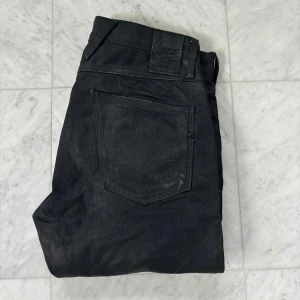 Replay svarta jeans slim fit - Svarta jeans från Replay med slim fit och klassisk femficksdesign. Byxorna har dragkedja, bälteshällor och Replay-logga på fickan. Materialet är jeans med en lätt glansig finish som ger en cool vibe. Passar dig som gillar stilrena och moderna jeans.