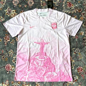 Vit och rosa Nike Dri-Fit fotbollströja - Snygg fotbollströja från Nike i Dri-Fit material, vit med rosa detaljer och motiv av Kristusstatyn i Rio de Janeiro. Kortärmad med rund hals och tryckt Nike-logga samt klubbmärke på bröstet. Perfekt för dig som gillar unik design och sportig stil.