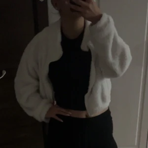 Vit croppad teddyjacka - Säljer en fluffig vit teddyjacka med croppad passform och långa ärmar. Jackan har en mjuk och gosig känsla, perfekt för dig som gillar att sticka ut med en cozy vibe. Enkel att matcha med både jeans och kjol.
