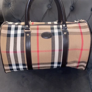 Burberry - Säljer en vintage gammal Burberrys of london handväska med det ikoniska rutiga mönstret i beige, svart, vitt och rött. Väskan har små defekter men inget som påverkar mycket. Den är min mormors gamla, vet inte om den är äkta! 