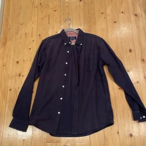 Mörkblå skjorta från Skill Casual Wear - Snygg mörkblå skjorta från Skill Casual Wear i storlek M. Klassisk button-down krage, vita knappar och en bröstficka. Tillverkad i mjuk bomull, perfekt för dig som gillar stilrena och enkla plagg. Långärmad modell med diskret rundad nederkant. Priset kan diskuteras