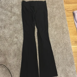 Svarta bootcut byxor från H&M - Snygga svarta bootcut byxor från H&M i storlek 152. Byxorna har hög midja, bred linning med två knappar och dragkedja. Materialet är mjukt och har lite stretch, vilket gör dem bekväma att bära. Perfekta för dig som gillar en klassisk och stilren look.