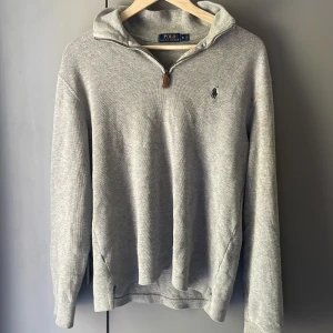 Grå half zip hoodie från Polo Ralph Lauren - Grå hoodie från Polo Ralph Lauren i storlek S med half zip och klassisk broderad logga på bröstet. Tröjan har huva, långa ärmar och är tillverkad i mjuk bomull. Perfekt för chill dagar och enkel att matcha med jeans eller joggers.