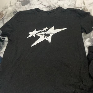 Oversized Svart t-shirt med vit stjärntryck - Svart t-shirt i storlek S med coolt vitt stjärntryck på bröstet. Klassisk rund hals och korta ärmar. Perfekt för dig som gillar grafiska prints och vill ha en enkel men snygg look. Materialet känns mjukt och skönt mot huden. Passar för S-XL