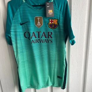 Barcelona Neymar Jr 11 fotbollströja - Snygg Barcelona fotbollströja från Nike med Neymar Jr och nummer 11 på ryggen. Tröjan är turkos med tunna horisontella ränder, korta ärmar och tryckta loggor från Qatar Airways, FIFA och Champions League. Materialet är lätt och andas, perfekt för match eller träning.