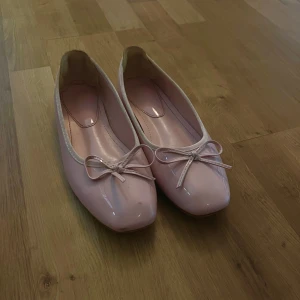 Rosa ballerinaskor med rosett - Snygga ljusrosa ballerinaskor med glansig finish och söt rosett framtill. Skorna har rund tå och platt sula, perfekta för dig som gillar en feminin och enkel stil. Passar till både jeans och klänning för en chill look.