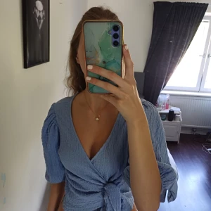Blå blus från Monki - Säljer en ljusblå blus från Monki med puffiga korta ärmar och snygg knytning framtill. Blusen har en ribbad, lite krinklad struktur. Den är croppad i modellen. Perfekt för dig som gillar att va lite ned unik och kanske sticka ut lite. Den är dupetfin men inte min smak ❤️ storlek M/S