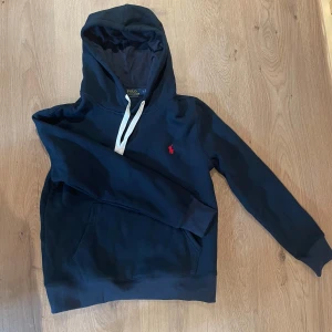 Mörkblå hoodie från Polo Ralph Lauren - Snygg mörkblå hoodie från Polo Ralph Lauren med  röd logga. Änvänd några gånger men säljer eftersom den sitter lite tajt på mig