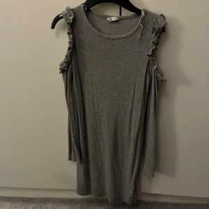 Grå ärmlös klänning med volang - Supersöt grå klänning från Cubus i mjukt ribbat material. Ärmlös modell med volangdetaljer längs axlarna som ger en extra touch. Rund halsringning och avslappnad passform. Passar dig som bär storlek XS/XXS. Skriv om ni vill se den på. 