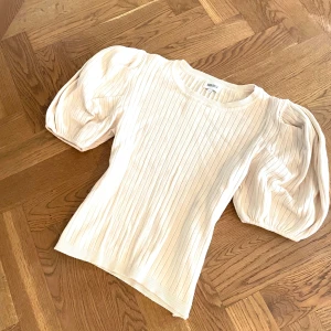 Ribbad beige topp med puffärm - Säljer en ribbad topp i ljus beige färg med puffiga kortärmar. Tröjan har rund hals och är tillverkad i mjuk bomullsmix. Perfekt för dig som gillar stilrena detaljer och volym vid axlarna.