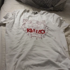 Vit Kenzo t-shirt med tigerbroderi - Vit t-shirt från Kenzo med ikoniskt tigerbroderi och röd Kenzo-logga på bröstet. Rund hals och korta ärmar. Broderade detaljer ger en unik vibe. Perfekt för dig som vill sticka ut med ett snyggt streetwear-plagg.