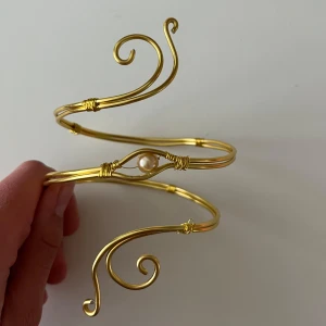 Guldfärgat armband vacker pärldetalj - Unikt armband i guldfärgad metall med snygga snirkliga former och en vit pärla i mitten. Armbandet är stelt och har en cool, bohemisk vibe som sticker ut. Perfekt accessoar för dig som vill ha något annorlunda och trendigt på armen.💗.    Finns även customs!!skicka gärna idéer eller bilder så kan vi nog lösa det💗