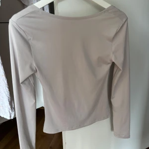 Beige långärmad topp med öppen rygg - Snygg beige långärmad topp med en cool öppen rygg och draperad detalj baktill. Tunn och mjuk, perfekt att styla med jeans eller kjol. Färgen är neutral och passar till allt, och den har en slim passform som sitter snyggt på kroppen.