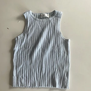 Ljusblå ribbad linnetopp från H&M - Snygg ljusblå linnetopp från H&M med vertikala ribbade ränder. Toppen är ärmlös och har en rund halsringning. Perfekt för dig som gillar enkel och stilren design med lite struktur. Materialet är mjukt och skönt bomull.