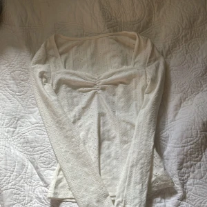 Vit spetsblus från SHEIN XS - Supersöt vit blus från SHEIN i storlek XS. Blusen har långa ärmar, spetsdetaljer och en v-ringad urringning med rynk framtill. Materialet är mjukt och stretchigt med broderade hålmönster som ger en romantisk vibe.