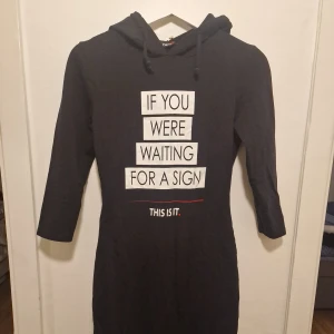 Svart hoodieklänning med tryck - Svart klänning med huva för en mer chill och avslappnad stil. 