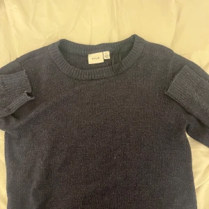 Mörkblå stickad tröja från VILA - Mysig mörkblå stickad tröja från VILA i storlek S. Tröjan har rund hals och långa ärmar med ribbade muddar. Perfekt för kyliga dagar och enkel att matcha med jeans eller kjol. Materialet är mjukt och ger en skön känsla mot huden.