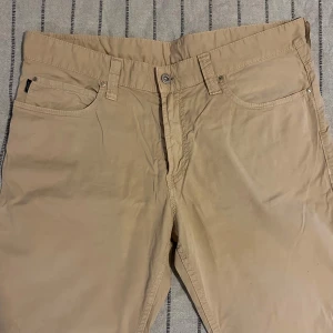Beige chinos från Armani Jeans - Armani Jeans chinos – beige, strl 34 Snygga chinos från Armani Jeans i klassisk femficksdesign med silverfärgad logga på bakfickan. Raka ben och normal passform i mjuk bomull. I mycket bra skick! Perfekta för dig som gillar stilrena och exklusiva detaljer.