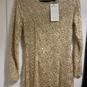 Champagnefärgad långklänning med paljetter - Säljer en maxilång klänning från Splendor i champagnefärgad ton, täckt med glittriga paljetter och ett unikt spetsmönster. Klänningen har lång ärm och rund halsringning, perfekt för dig som vill sticka ut med en elegant och lyxig look. Storlek xs men passar mig som är storlek S. Aldrig använd. 