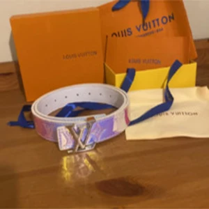 Louis Vuitton holografiskt bälte - Säljer ett Louis Vuitton bälte i holografiskt skinn med ikoniskt LV-spänne i silver. Bältet har en glansig yta som skiftar i blått, lila och grönt med präglade LV-monogram. Insidan är vit och bältet kommer med originalförpackning och dustbag.