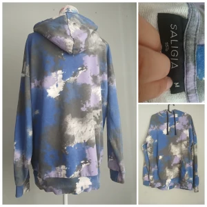 Unik SALIGIA hoodie i blått/lila tie-dye – streetwear vibes & supermysig! 🔥 - Cool och bekväm hoodie i tie-dye/abstrakt mönster med nyanser av blått, lila, grått och vitt. Perfekt för dig som vill sticka ut med en streetwear-inspirerad look.  ✅ Märke: SALIGIA - lager157  ✅ Storlek: M (passar även S för oversized look) ✅ Mjuk och skön kvalitet ✅ Känguruficka och dragsko i luvan ✅ Fint skick – knappt använd  📍 Passar både vardag, mysdagar och som statementplagg.