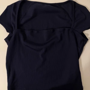 Mörkblå ribbad croppad topp - Snygg mörkblå croppad topp med ribbad struktur och korta ärmar. Toppen har en enkel och stilren design som passar perfekt till jeans eller kjol. Materialet är mjukt och stretchigt för en bekväm passform.
