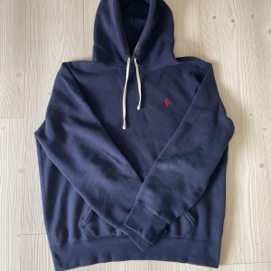 Ralph lauren hoodie  - Stilren ralph lauren hoodie i en väldigt stilig och trendig mörkblå färg. Hoodien har broderat Ralph lauren märke på bröstet, och vita snören. Storlek S sitter som S/M. Tyvärr så finns det en gulfläck på insidan av luvan, går dock att dölja och kanske går att få bort i tvätten (inte testat själv) så absolut inte värsta, Utöver det är tröjan i ett väldigt bra skick samt väldigt bekväm. Men ändå därav det billiga priset. Vid frågor är det bara att höra av sig!