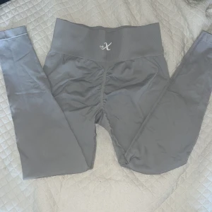 Grå scrunch träningsbyxor från X - Snygga grå träningsbyxor med scrunch-detalj bak och bred, ribbad midja från X. Perfekta för gymmet. Stretchigt material som sitter tight och framhäver formerna. Diskret logga framtill på midjan! 😇