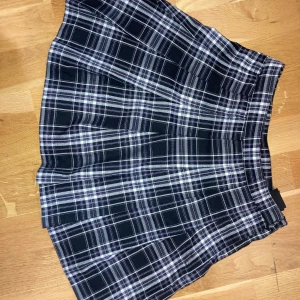 Svartvit lila rutig kjol från H&M - Fin svart kjol med vita och lila rutor. Knapp och dragkedja på sidan, inga defekter. Säljer för att den är för liten