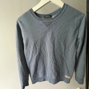 Blå sweatshirt från Polo Ralph Lauren - Snygg blå sweatshirt från Polo Ralph Lauren i storlek M10/12år. Tröjan har rund hals, långa ärmar och en diskret etikett med RP&CO vid nederkanten. Mjuk bomullskänsla och klassisk passform, perfekt för chill dagar. Enkel och stilren design utan mönster.