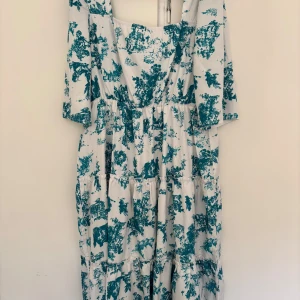 Vit och blå långklänning med mönster - Säljer en flowy långklänning med vitt tyg och blått mönster. Halvlånga ärmar och volangdetaljer längs kjolen. Perfekt för dig som gillar romantisk stil och vill sticka ut med ett unikt print.