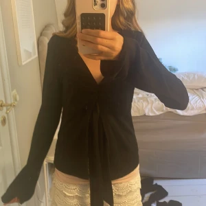 Svart omlottopp med knyt från Gina Tricot - Svart omlottopp från Gina Tricot i storlek S. Toppen har lång ärm, v-ringning och snygg knytning framtill. Materialet är mjukt och stretchigt. Enkel men ändå trendig design.