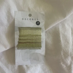 Guldiga hårnålar från Decorus - 30-pack guldiga hårnålar från Decorus, perfekta för att fixa frisyren eller sätta upp håret snyggt. Smala och stilrena med en klassisk form som passar till alla tillfällen.