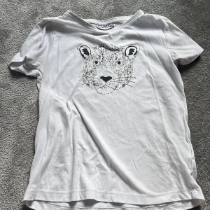 Vit t-shirt med leopardtryck Red & Blu - Vit t-shirt från Red & Blu med ett coolt leopardansikte tryckt på bröstet. Klassisk rund hals och korta ärmar. Mjuk och skön bomull som passar perfekt till jeans eller shorts. Snyggt djurmotiv som ger en chill vibe.