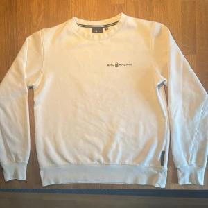Vit/ljusbeige Sail Racing sweatshirt i bomull - Snygg vit sweatshirt från Sail Racing i storlek S. Tröjan har rund hals, långärmade ärmar och svart ”Sail racing logga” tryckt på bröstet. Tillverkad i bomull med smalare passform vid ärmarnas slut och nederkant. Perfekt för chill dagar och enkel att matcha med jeans. Hoppas du blir nöjd!