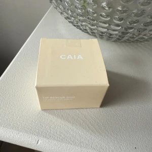 CAIA Lip Rescue Duo läppkit - Oöppnad! CAIA Lip Rescue Duo innehåller en läppmask och en läppskrubb, perfekt för att återfukta och exfoliera läpparna. Kommer i en stilren beige kartong med vit text. Passar alla hudtyper och är ett måste för mjuka, återfuktade läppar.