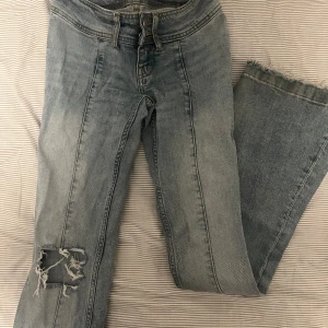 Ljusblå slitna jeans med rå kant - Ljusblå jeans med coola slitningar på benet och rå, fransig kant nedtill. Klassisk femficksmodell med synliga sömmar och dragkedja. Perfekta för en avslappnad och trendig look. Ett litet hål som knappt syns vid midjan