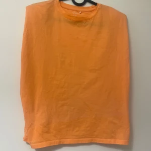 Orange t-shirt från Name It - En basic orange t-shirt från Name It. Den har ett lager tjocking i axlarna, färgen är lite mer pastellfärgad i verkligheten. Använt 2 gånger. Pris kan diskuteras