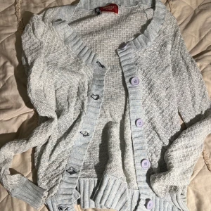 Ljusblå kofta med lila knappar - Söt ljusblå stickad kofta från Soulful med bred ribbad kant och lila knappar framtill. Koftan har långärmad design och ett diskret mönster i stickningen. Perfekt att slänga över en topp för en chill look.