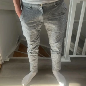 Grå chinos från Jack & Jones - Snygga grå/blå chinos från Jack & Jones i storlek 29/32. Byxorna har en smal passform, klassiska fickor fram och bak samt bälteshällor. Perfekta för en clean och stilren look. Materialet känns lätt och passar bra till vår och sommar.