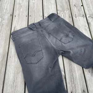 Replay Anbass grå jeans slim fit - Snygga grå Replay Anbass jeans med slim fit och klassisk femficksdesign. Jeansen har svarta detaljer, diskret Replay-logga vid fickan och coola sömmar på bakfickorna. Perfekta för dig som gillar en modern och stilren look. Längden är 32 och bredden är 32! Nypris 1800kr!