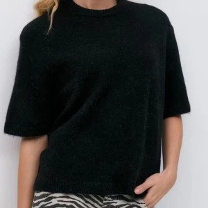 Svart stickad tröja med kort ärm - En svart stickad tröja med rund hals och korta ärmar. Tröjan har en avslappnad passform och är perfekt för lager-på-lager. Mjuk och skön känsla, passar till både jeans och kjol.