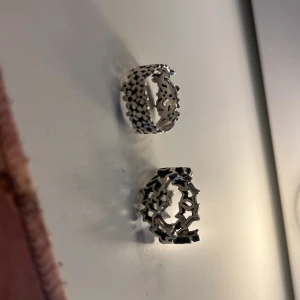Två breda silvriga ringar med stjärnor och blommor - Säljer två chunky silvriga ringar i cool design. Den ena ringen har utskurna stjärnor runt om och den andra har ett mönster av små blommor. Båda är öppna baktill så de är justerbara i storlek. Perfekta för dig som gillar statement-smycken!