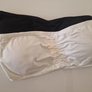 Svart och vit bandeau tubtopp - Två bandeau tubtoppar i svart och vitt, perfekta för sommaren till klänningar och linnen. De är ärmlösa och har lätt rynk framtill för snygg passform. Mjukt bomullsmaterial som känns skönt mot huden.