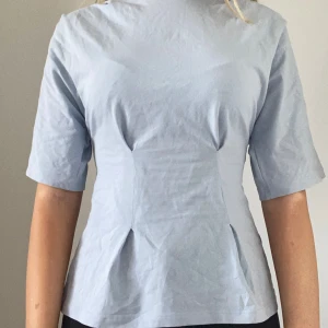 Ljusblå figursydd blus med veck - Säljer en supergullig ljusblå topp!  Den är figursydd med veck. Andra bilden är inte min 💗Är använd men inte trasig eller så, säljer då den inte används.