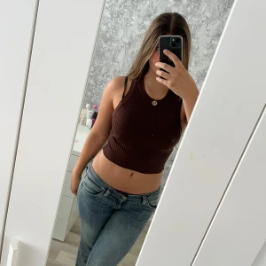 Brun ribbad croppad linne - Säljer en brun croppad ribbad topp från Divided. Toppen är ärmlös med hög halsringning och sitter tight mot kroppen. Vid frågor hör av dig!