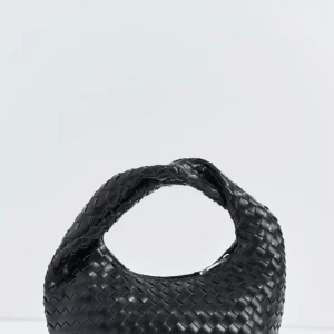 Svart flätad handväska i skinn ifrån Gina  - Stilren svart handväska med flätad design och rundad form. Väskan är tillverkad i skinn och har ett kort handtag som gör den enkel att bära i handen eller på armen. Perfekt accessoar för att lyfta din outfit med en trendig touch.
