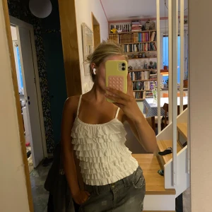 Vit Volangtopp  - Supersöt vit linnetopp med smala axelband och flera lager volanger framtill. Toppen är figurnära och har en lätt croppad passform, perfekt för varma dagar. Något insydd för mer figursydd passform💕🌺Tror den kan vars väldigt snygg tex på någon med lite boobs