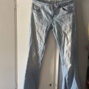 Ljusblå bootcut jeans med rå kant - Säljer ett par ljusblå jeans med bootcut-modell och rå, fransig kant upptill. Jeansen har klassiska fem fickor och stängs med knapp och dragkedja. Perfekta för dig som gillar en avslappnad och trendig look.