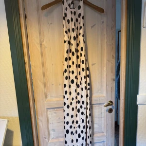 Prickig långklänning med knyt i nacken - Supersnygg långklänning i ljus beige med stora svarta prickar. Klänningen har halterneck med knyt i nacken och öppen rygg. Den är köpt via ASOS och är helt oanvänd! 